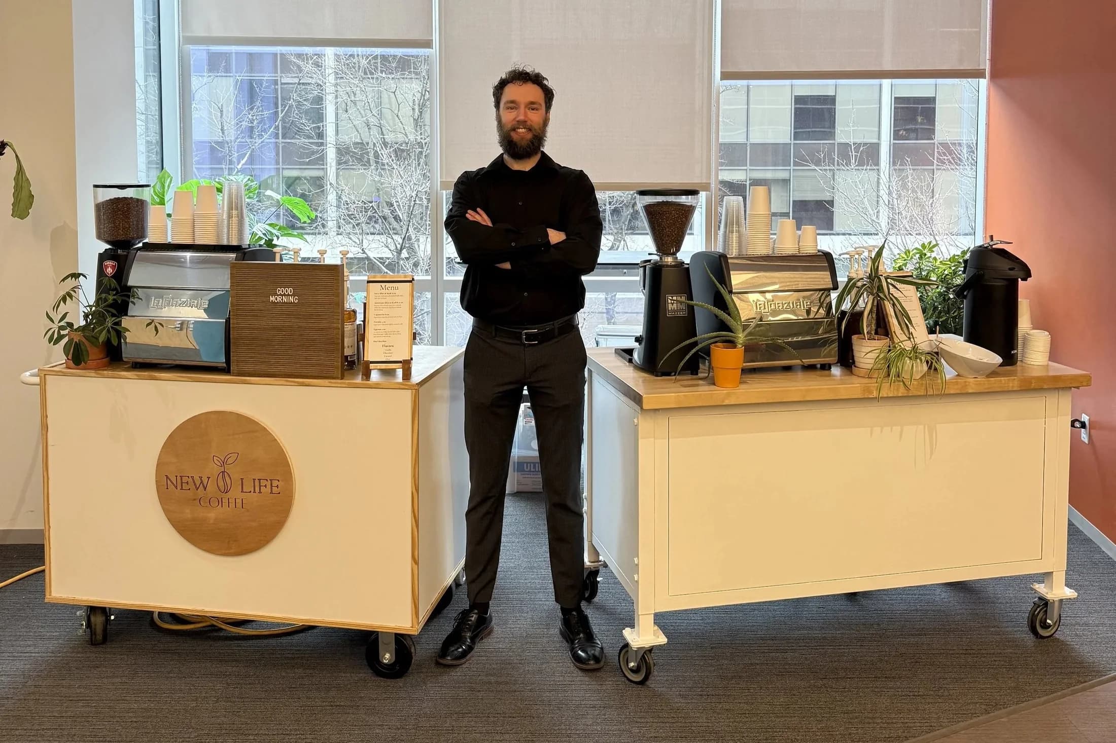 New Life Coffee Company barista standing beside two mobile coffee carts in a corporate office with floor-to-ceiling windows