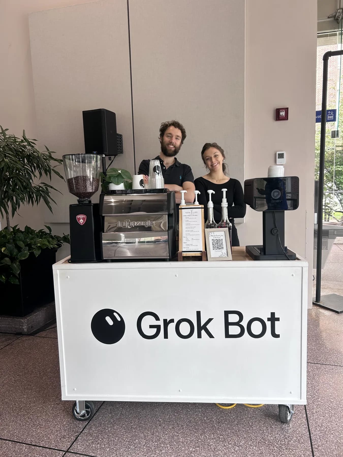 New Life Coffee Company baristas behind a Grok Bot branded espresso cart in an office lobby