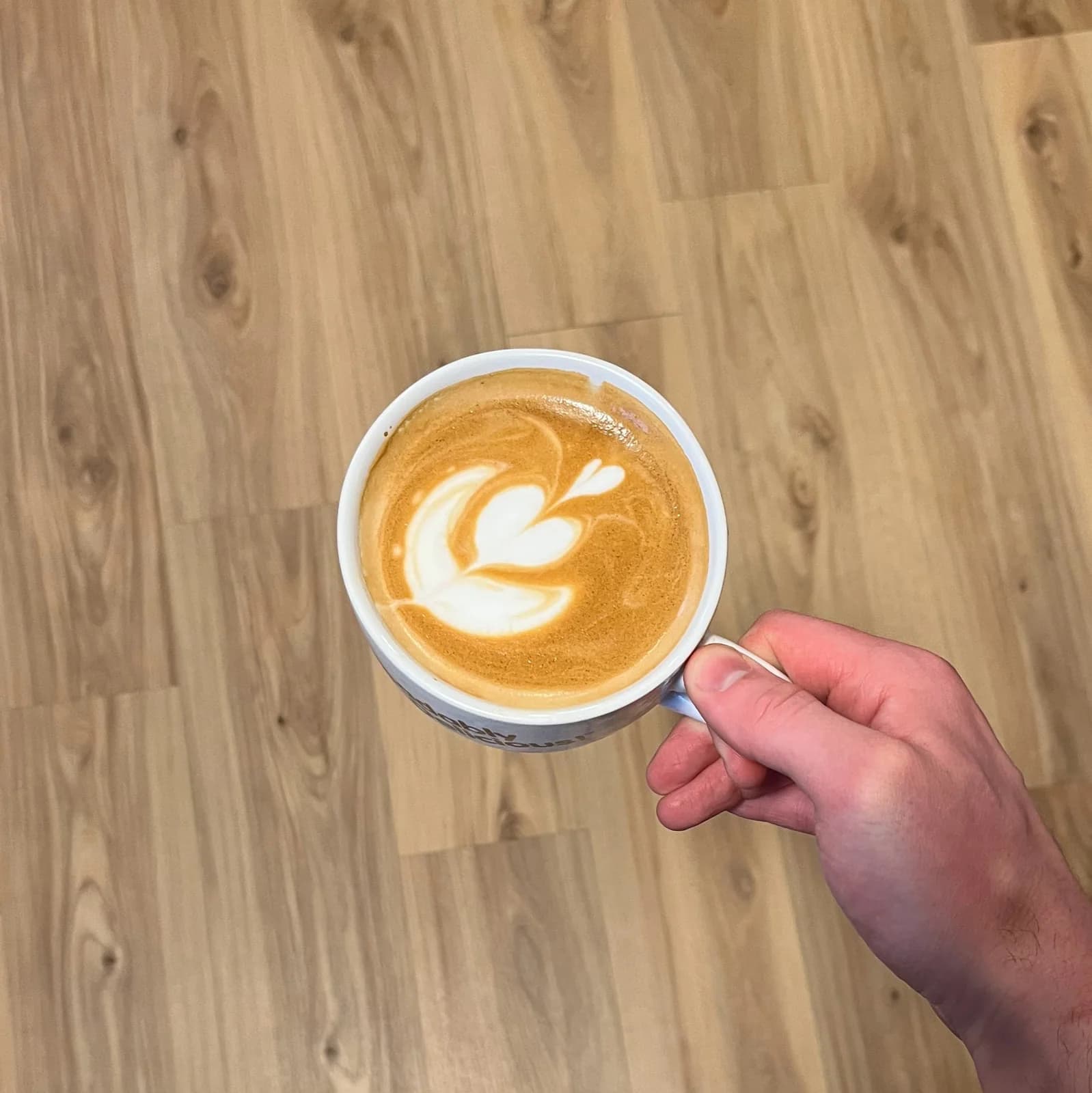 Hand holding a latte with rosetta latte art poured by a New Life Coffee Company barista